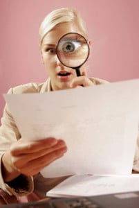 work environment- woman with a magnifying glass over some paperwork in modern office-on pink